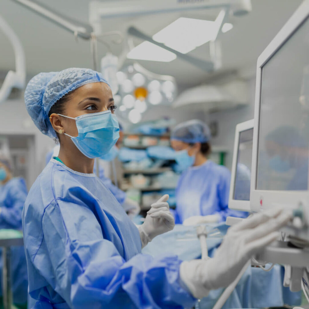 A masked nurse in a surgical gown adjusts a piece of medical equipment in a facility representing Saint Luke’s Health System.