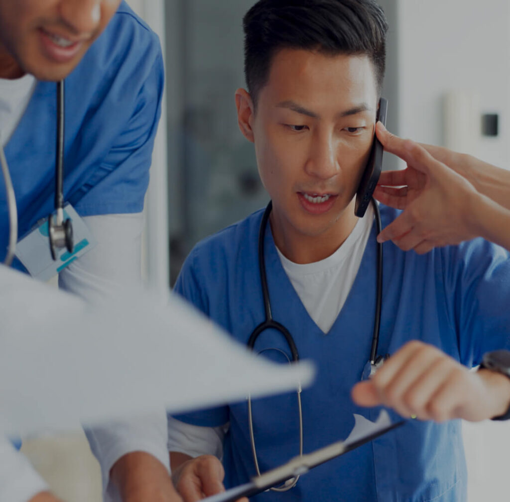 A harried doctor takes a phone call and reviews paperwork in a facility representing Boston Medical Center